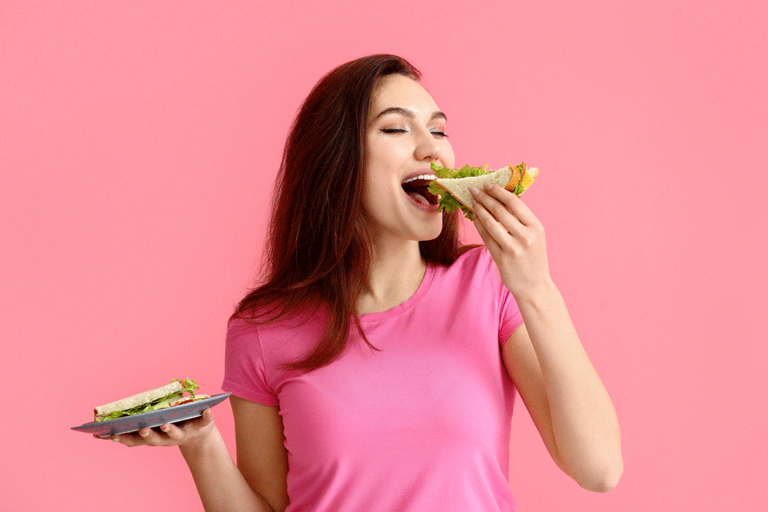 mujer comiendo feliz, con blusa rosa y fondo color rosa