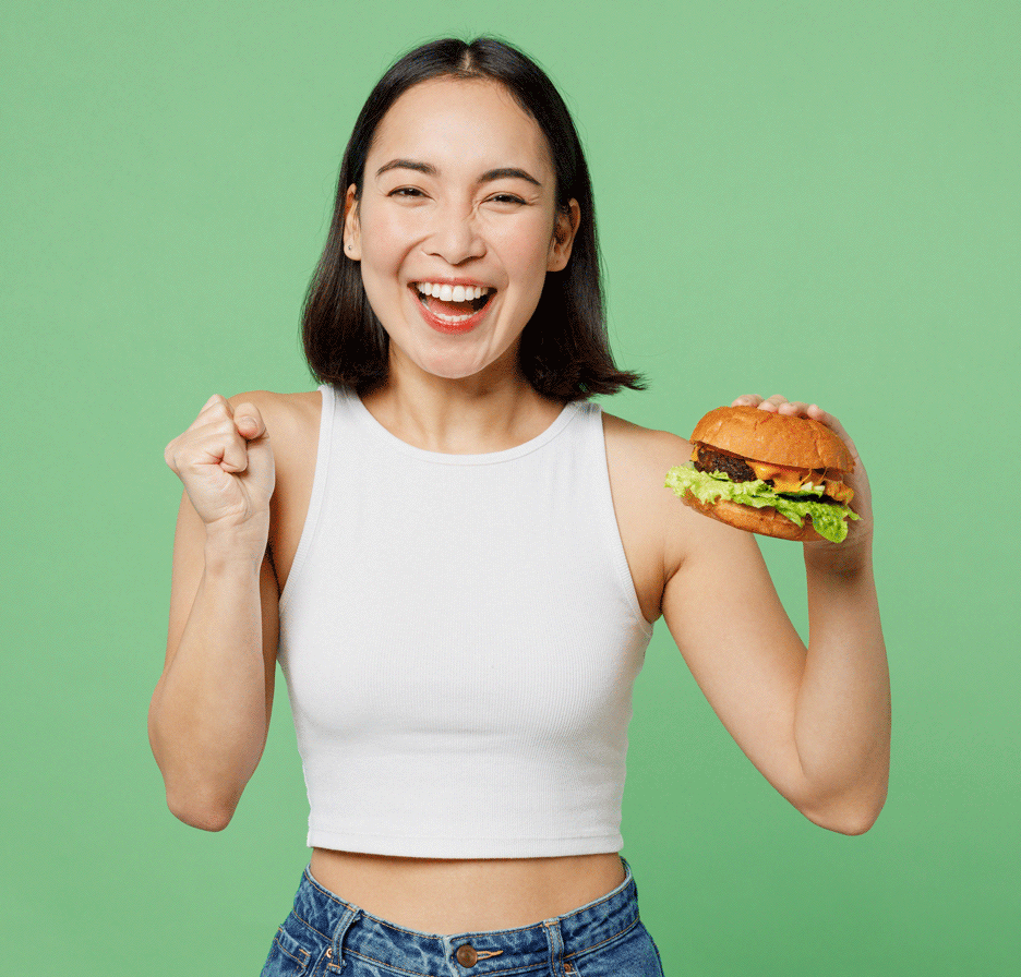 mujer joven sosteniendo una hamburguesa y sonriendo con un fondo verde claro